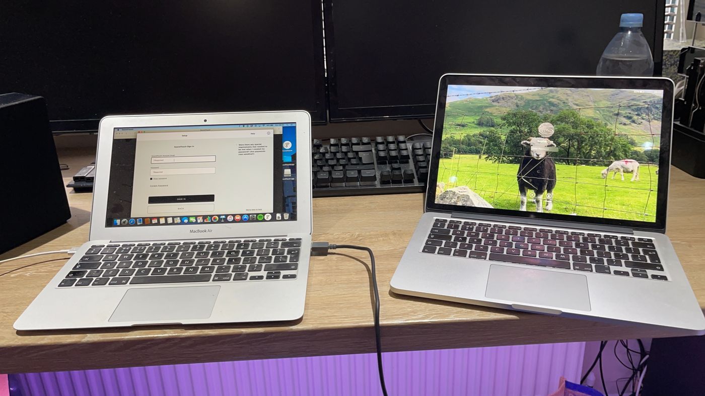 Two MacBooks on a repair bench being set up and tested